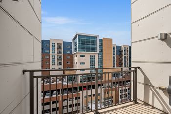 A balcony with a metal railing overlooks a parking lot and buildings.